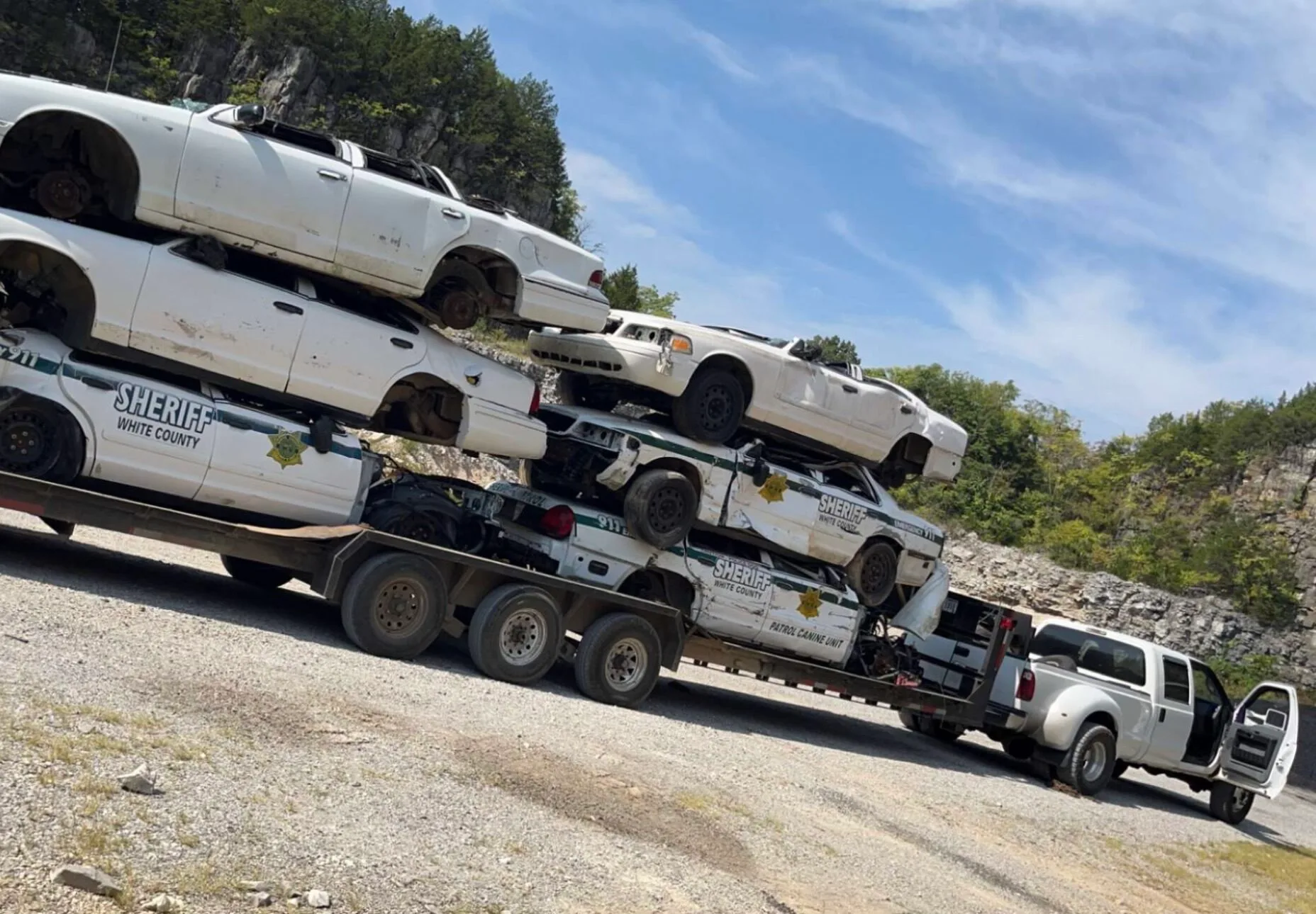 A stack of old sheriff vehicles being towed on a flatbed trailer by Ohio Junk Cars