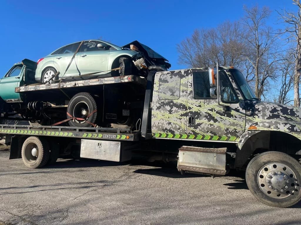 A flatbed truck with a junk car on top being towed by Ohio Junk Cars