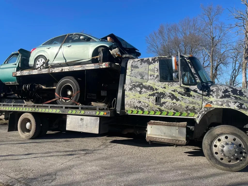 A flatbed truck with a junk car on top being towed by Ohio Junk Cars